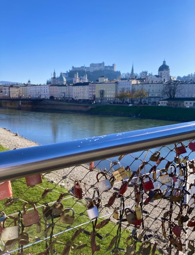 A bridge with padlocks in the foreground, in the background a river and fortress