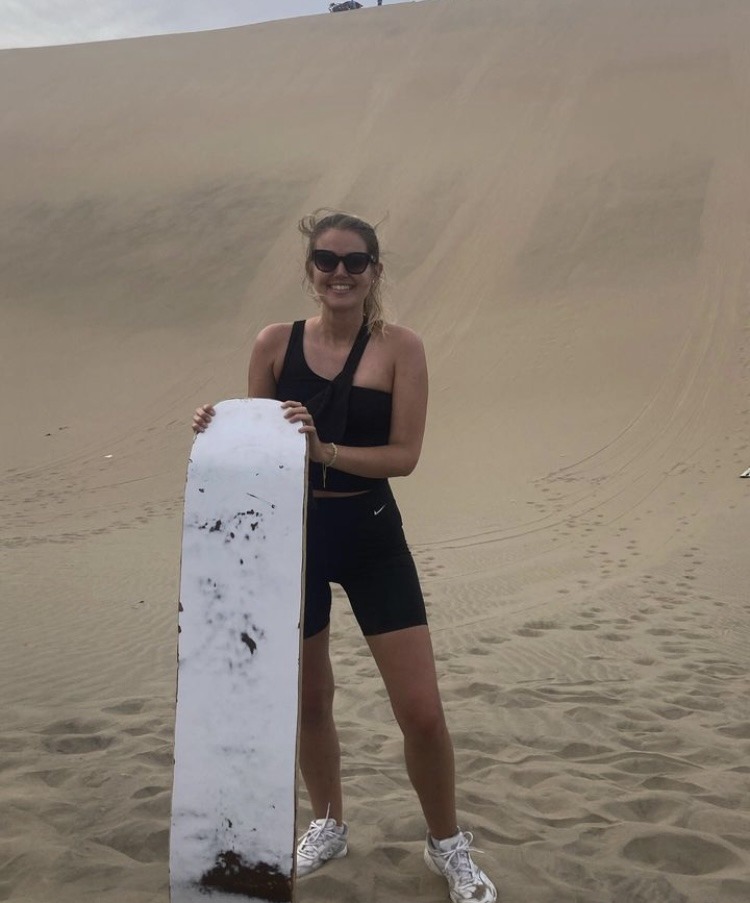 girl holding board in front of sand dune